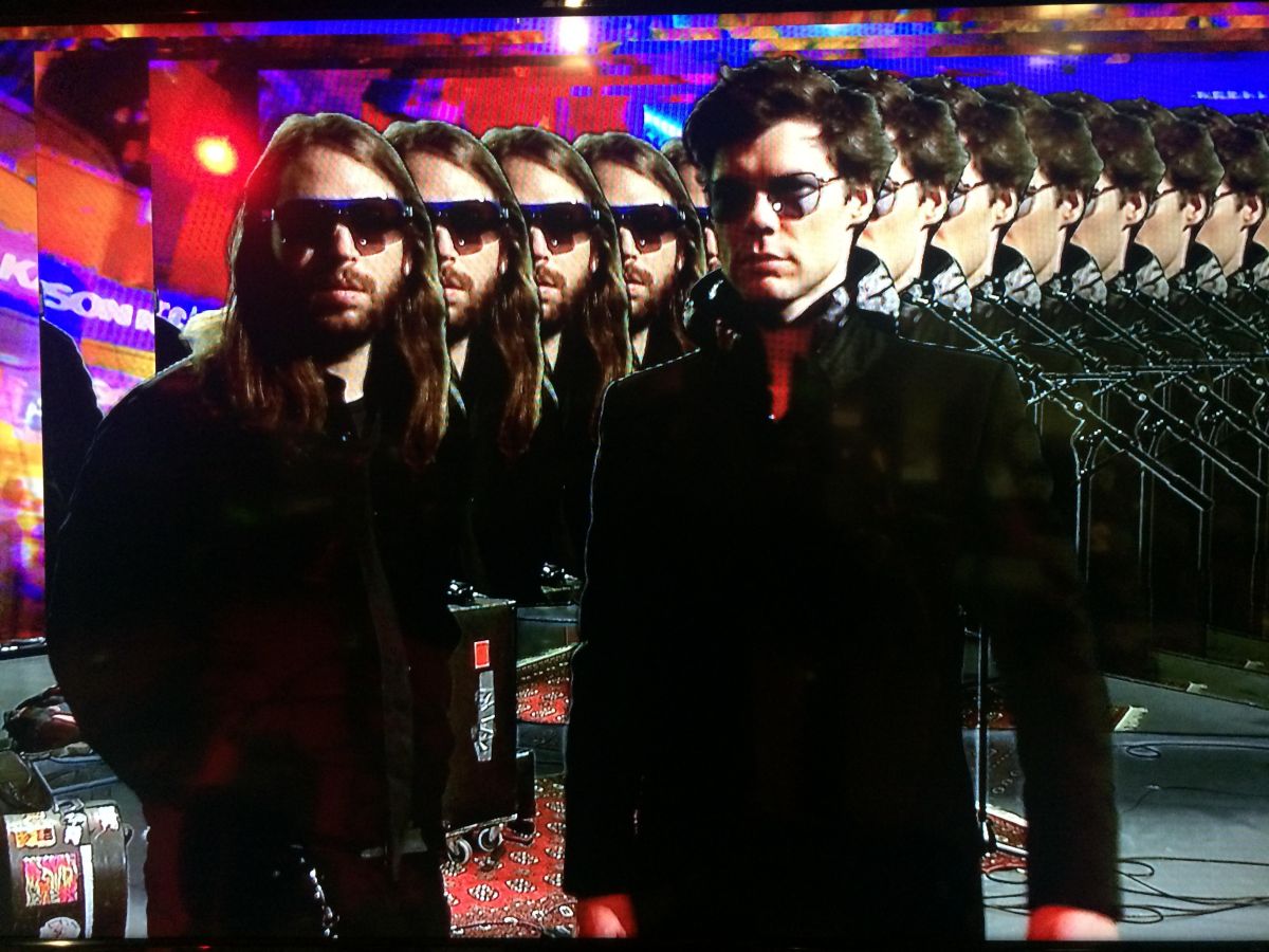 Zwei Männer mit Sonnenbrillen vor einem psychedelischen Hintergrund